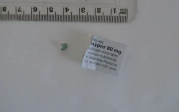 Fragment de comprimé d'oxycodone à côté de l'étiquette d'Oxypro 80 mg à libération prolongée